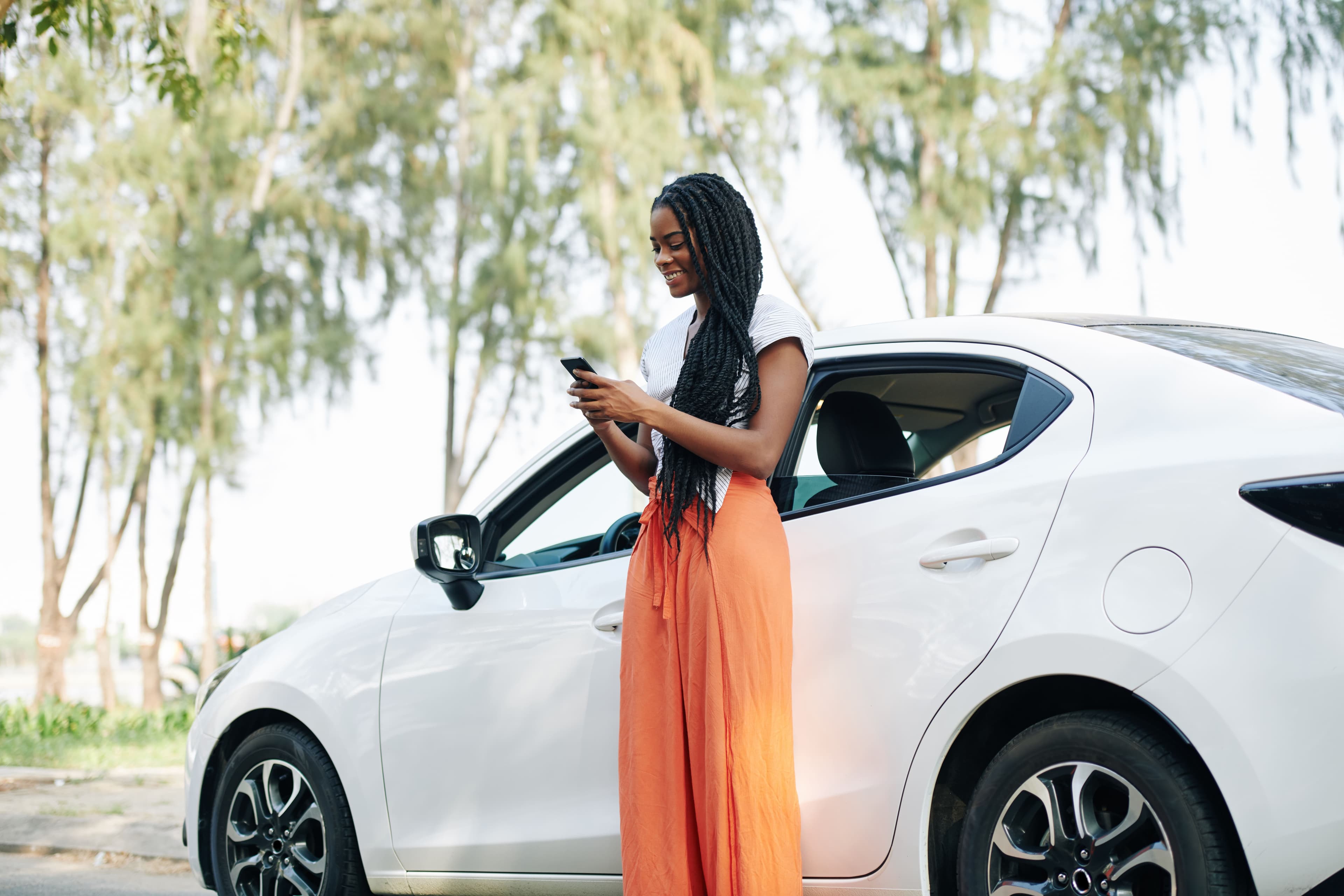 Woman using phone next to white car